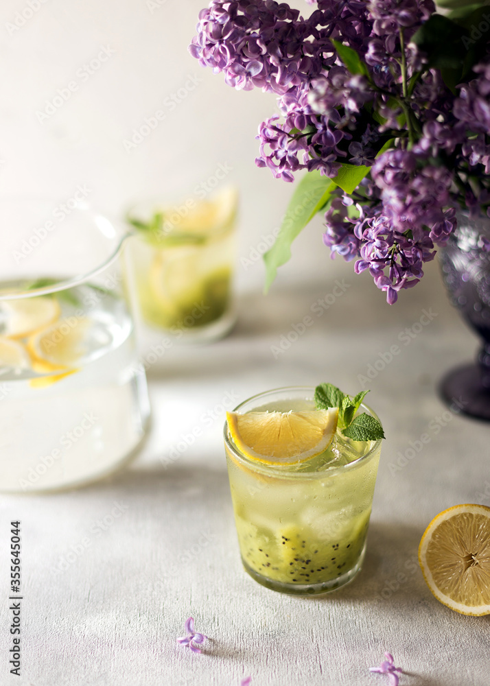 Fresh summer lemonnad with mint and kiwi stands on the table. Nearby is a bouquet of lilacs in a purple vase. Fresh summer lemonnad with mint and kiwi stands on the table. Nearby is a bouquet of lilacs in a purple vase.
