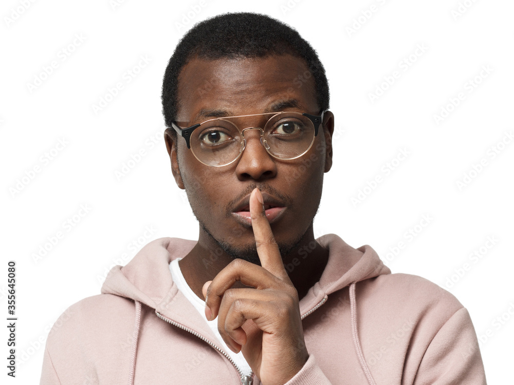 Shh! Young african man wearing round eyeglasses and pressing index finger to lips as if asking other to keep silent about exciting secret or data, isolated on white background Shh! Young african man wearing round eyeglasses and pressing index finger to lips as if asking other to keep silent about exciting secret or data, isolated on white background