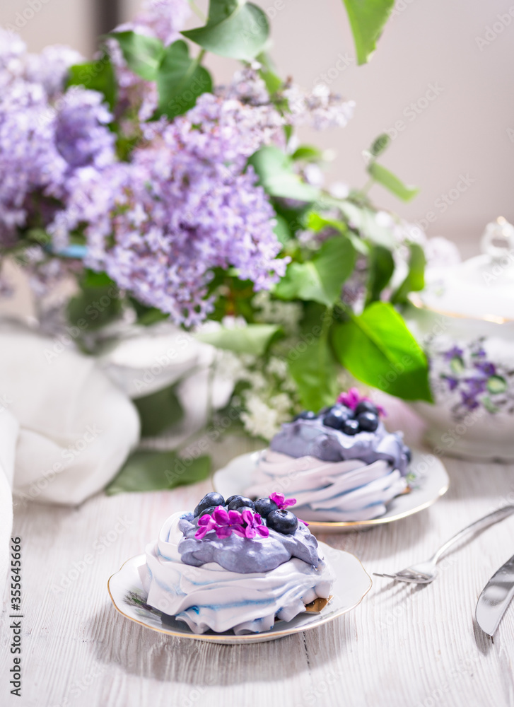Porcelain plate with meringue with whipped cream decorated with lilac flowers on wooden background