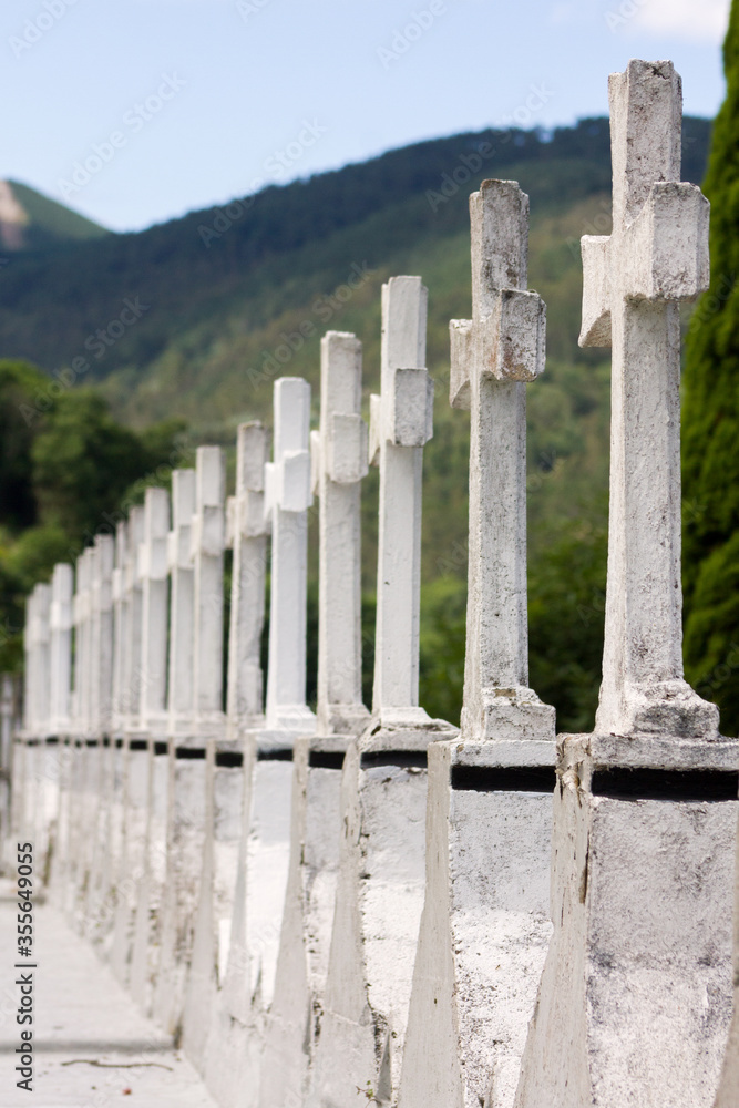 Asturias, Spain. Row of white stone crosses in a cemetery with green mountains in the background.