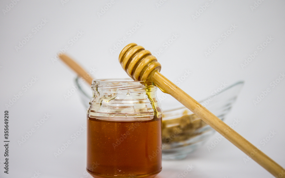 Glass jar with honey and a wooden stick on a white background Glass jar with honey and a wooden stick on a white background
