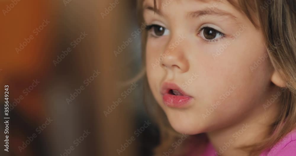 Adorable little girl in the sunlit living room watching tv and eating cereals