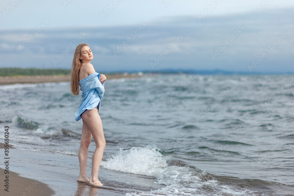 Beautiful young blonde girl in a blue shirt relaxing on the sea