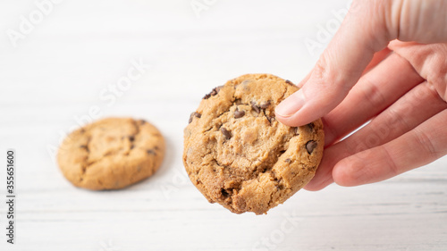 Chocolate chip cookie in hand. Hand holding cookie with chocolate drops on white wooden background. American cookie