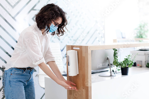 Disinfectant liquid in office. Disinfection hands with sanitizer in public place. Hygiene, staff safety. Protection employees on workplace. Receptionist in mask at reception in hotel during quarantine