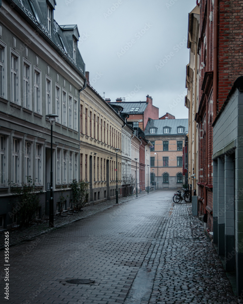 An empty cobblestoned street bordered with old colorful houses on a rainy day in Malmö, Sweden