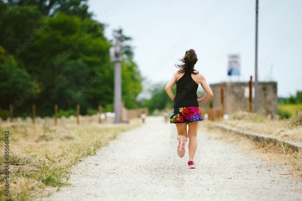Woman running alone on dirt road, greenway on her back