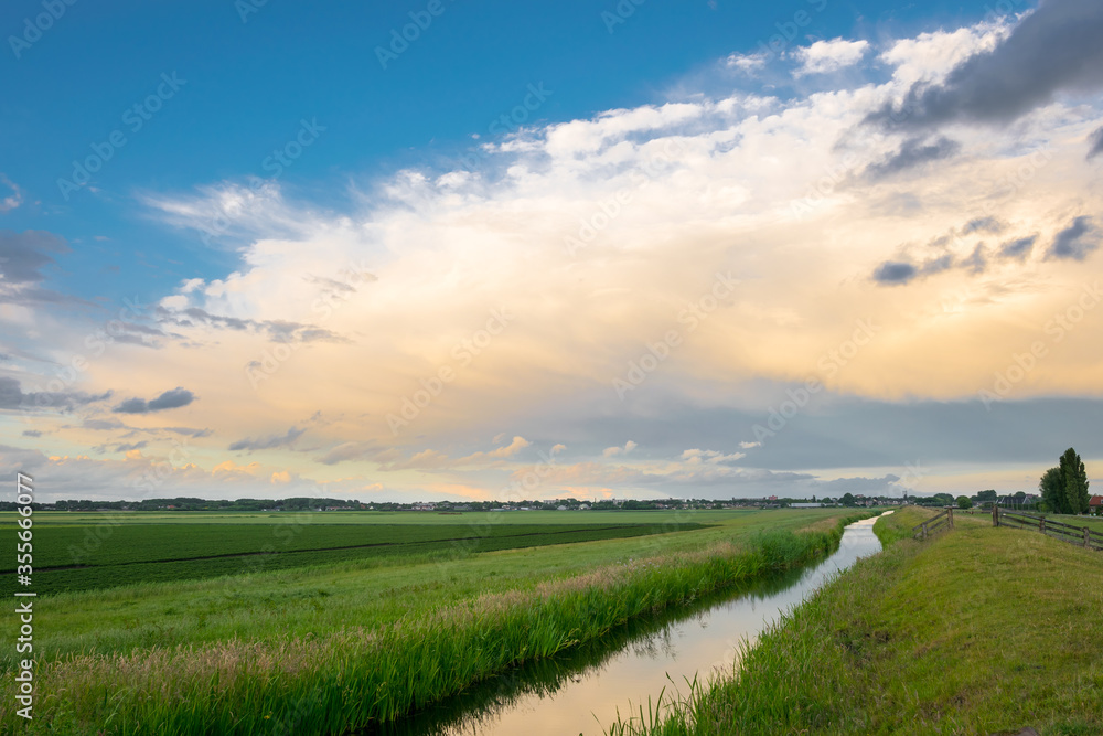 Obraz premium Anvil of a distant thundery shower is colorfully illuminated by the low sun