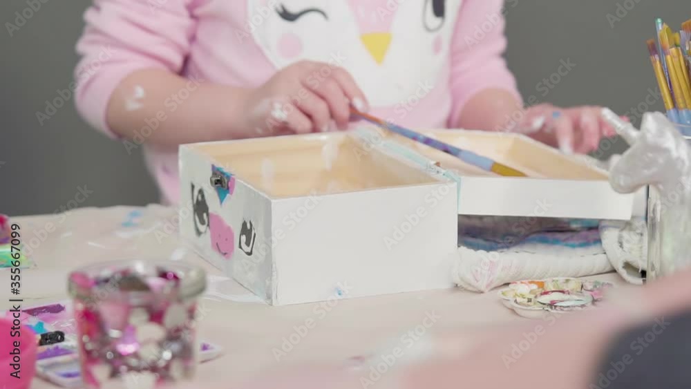 Little girl painting a white unicorn with acrylic paint on a wooden box. Little girl painting a white unicorn with acrylic paint on a wooden box.