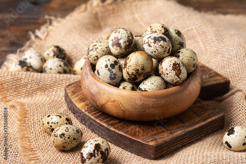 Fresh quail eggs in a wooden bowl on a brown wooden table. Raw quail eggs close-up on a culinary background. Concept of preparation for cooking