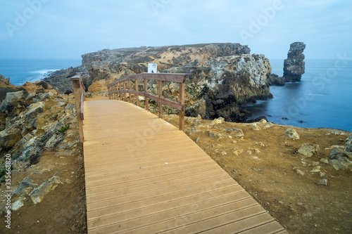 Long exposure seascape of the cliffs of Papoa island and wooden bridge way in Carvoeiro cape in a foggy morning, Atlantic coast, Portugal photo