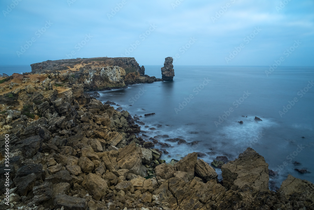 Long exposure seascape of the cliffs of Papoa island in Carvoeiro cape from the sea at sunrise in a cloudy day, Atlantic coast, Portugal