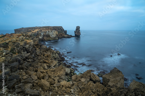 Long exposure seascape of the cliffs of Papoa island in Carvoeiro cape from the sea at sunrise in a cloudy day, Atlantic coast, Portugal
