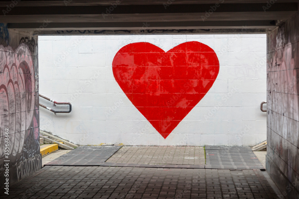 Fototapeta premium A big red heart is painted on a white wall. Street graffiti, street art expressing love