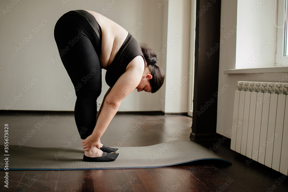 Obraz premium Fitness, home training, flexibility. Overweight woman doing stretching exercises on a fitness mat at her living room. Healthy lifestyle