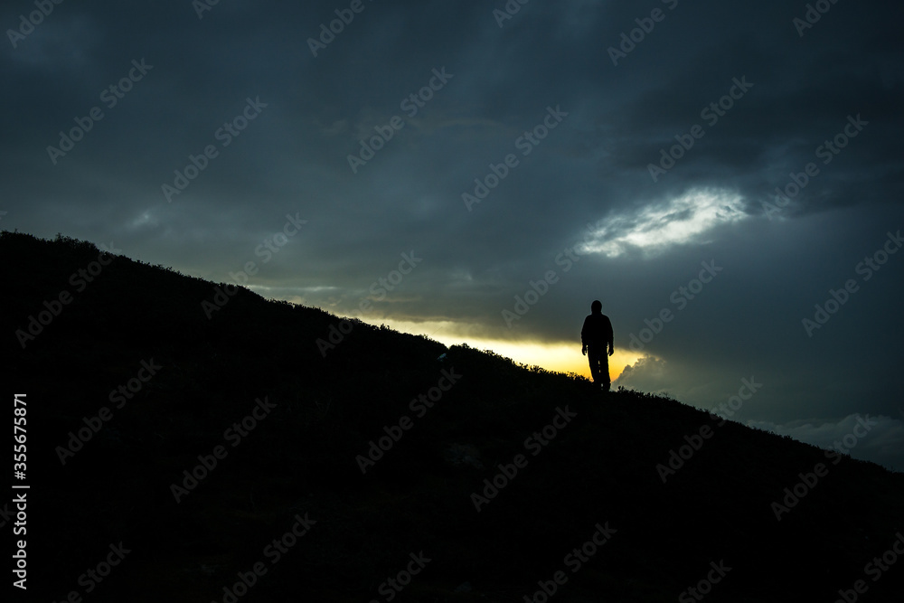 A lonely man standing on a dark mountain slope with ray of hope. A conceptual image of emotions, mental health, success, depression, wellbeing, mental health. 