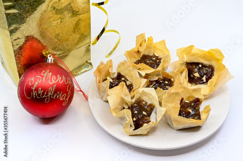 Filo pastry baskets with mincemeat on a white plate, with a Merry Christmas bauble and a gold gift bag photo