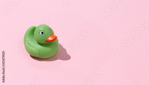 Unusual green rubber ducky toy on pastel pink background isolated with copy space