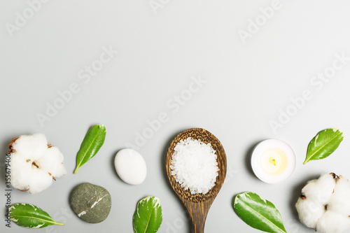  Bath salt in a wooden spoon, candle, green leaves, stone and cotton on a gray background. spa and beauty concept. flat lay, copy space.
