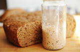 Freshly baked homemade rye-wheat whole grain bread and rye sourdough in a glass jar. Close up