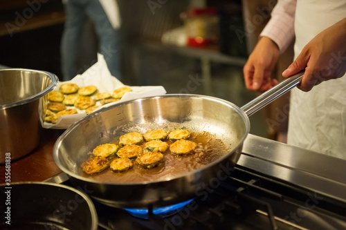 Man hands holding a frying pan, cooking zucchini rings.