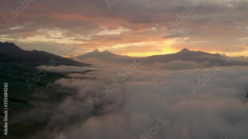 Aerial flies over a wall of clouds around Cotopaxi with beautiful sunset.