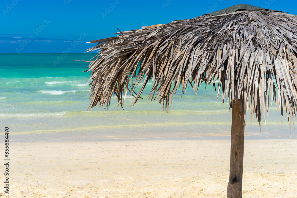 Cuba. Beach. A canopy of palm branches. Beach umbrella made of palm leaves. Umbrella on the background of an exotic beach. Shadow. Island Cuba Tourism. Caribbean landscape. Sand beach.