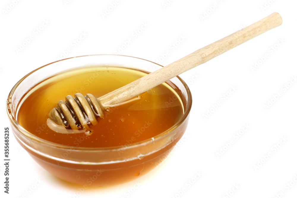 Honey in a bowl with a wooden stick isolated on a white background Honey in a bowl with a wooden stick isolated on a white background