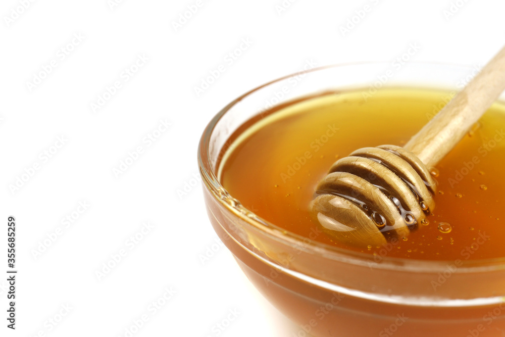 Honey in a bowl with a wooden stick isolated on a white background Honey in a bowl with a wooden stick isolated on a white background