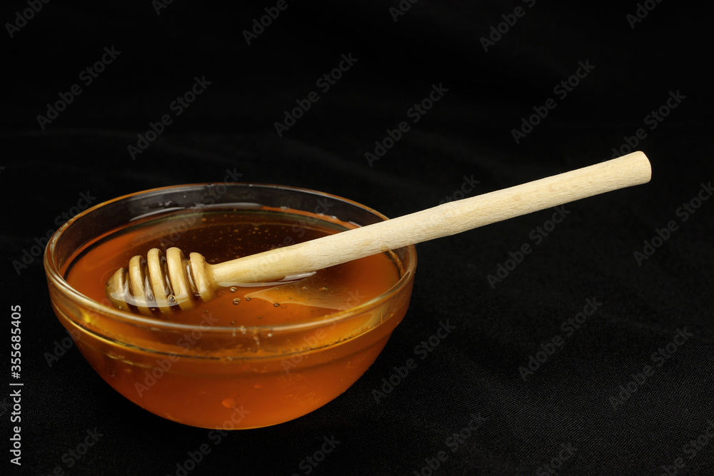 Honey in a bowl with a wooden stick on a black background Honey in a bowl with a wooden stick on a black background