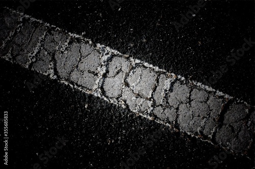 Detailed close-up of a deteriorated white traffic line painted on dark asphalt, revealing deep cracks and granular texture
