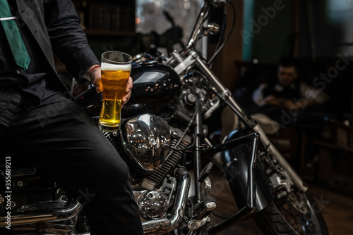 Biker sitting on a custom motorcycle with a glass of shiny craft beer. Chrome bike