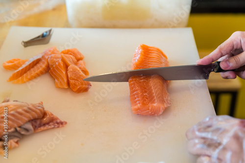 Chef use knife preparing a fresh salmon on a cutting board, Japanese chef in restaurant slicing raw salmon, ingredient for seafood dish. Chef with a knife cutting raw salmon.