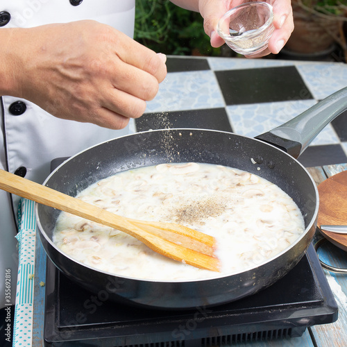 Chef putting pepper in the pan for cooking mushroom cream soup