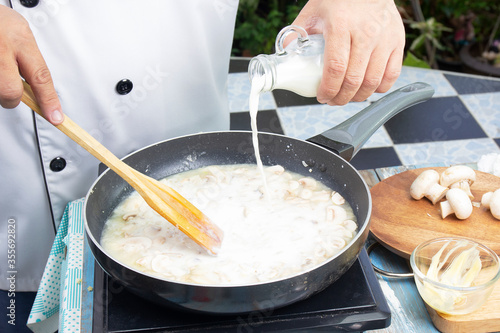 Chef pouring fresh milk the pan for cooking mushroom cream soup