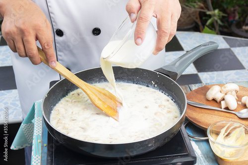 Fotografie, Obraz Chef pouring whipping cream in the pan for cooking mushroom cream soup