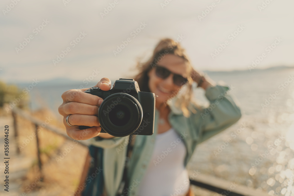 Obraz premium Close-up photo camera in the hand of a happy traveler woman by the sea, joy of vacation and travel