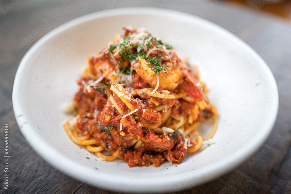 A Pasta/Spaghetti with shrimp and cheese that served in the white luxury dish, placed on wooden table. Italian food and special dish photo. Select focus on the food surface. A Pasta/Spaghetti with shrimp and cheese that served in the white luxury dish, placed on wooden table. Italian food and special dish photo. Select focus on the food surface.