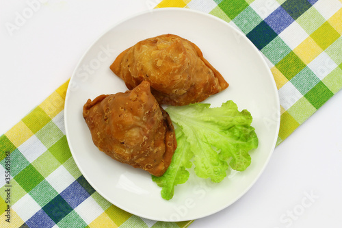 Two Indian samosas on green lettuce on white plate on checkered cloth 