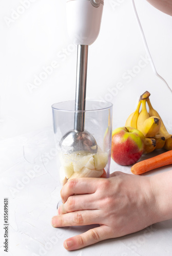 Step by step cooking smoothies. On a light background lies an apple, banana, carrot and a measuring cup. Male hands hold a blender and mix the ingredients in a glass. The concept of healthy nutrition.