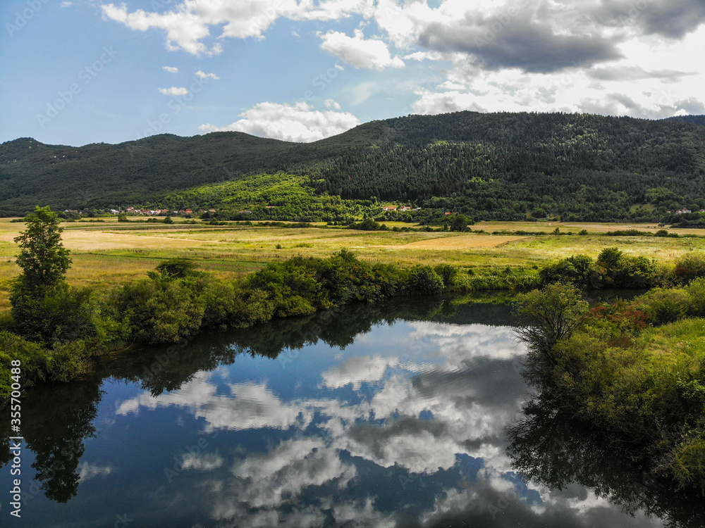 View of the Lika River in small village Donji Kosinj in Croatia. Water reflection of clouds.