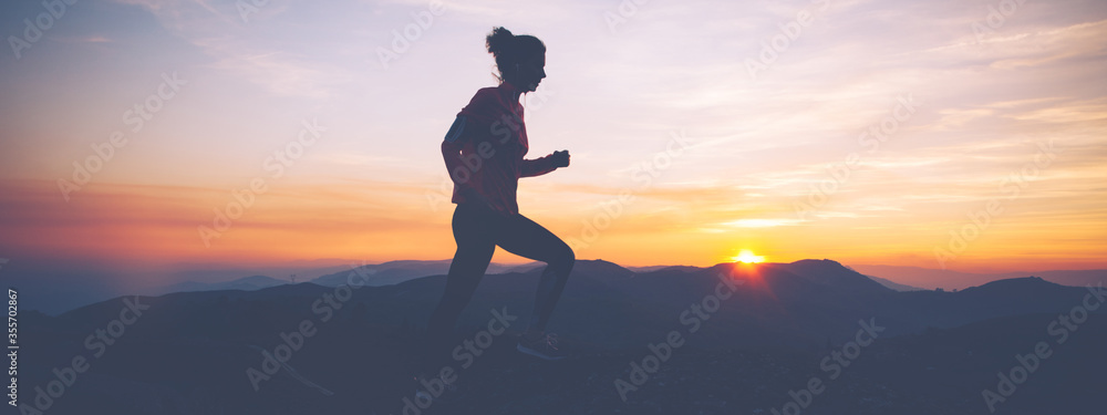 Silhouette of athletic woman finishes workout in the mountains at sunset. Sport tight clothes. Intentional motion blur.