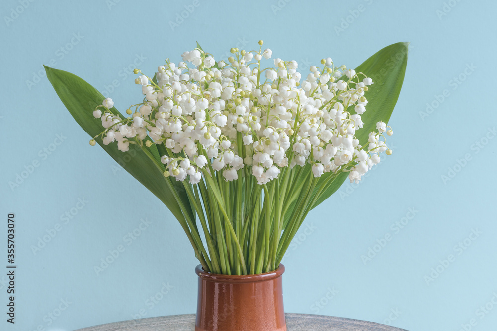 Flowers of lily of the valley (Convallaria majalis), small white bells in a vase on a turquoise background.