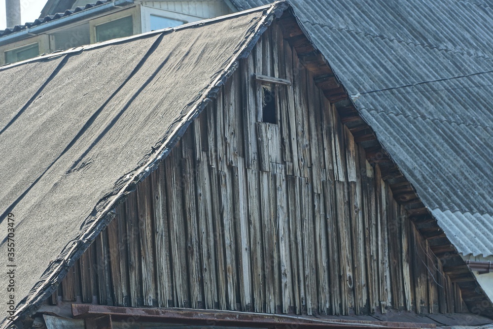 Naklejka premium gray old wooden attic of a rural house with a small window under a ruberoid roof