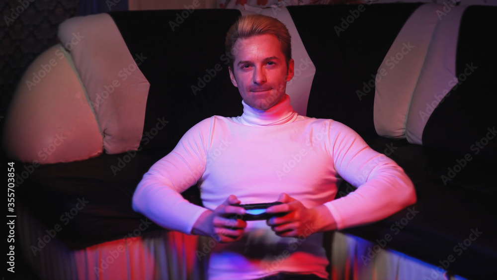 a bright young man plays a video game, is upset, is crazy about being angry that he lost against a sofa in a blue-red a bright young man plays a video game, is upset, is crazy about being angry that he lost against a sofa in a blue-red