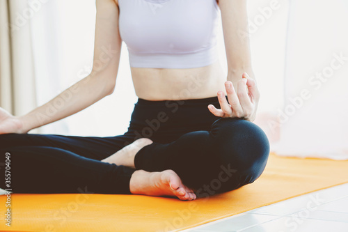 Fit young woman doing exercises of yoga seated Hand Mudra and meditates in living room at home,