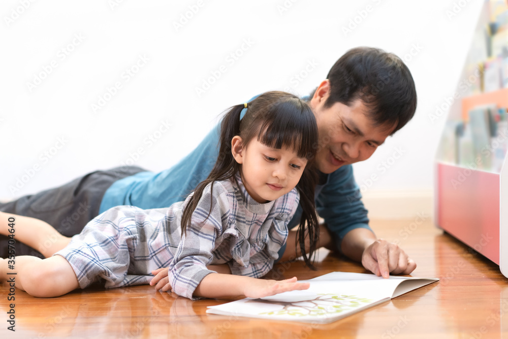 Asian little daughter and father is laying on the floor and reading the story book together in the room at home, concept of homeschooling and active learning for kid, new normal of education trending. Asian little daughter and father is laying on the floor and reading the story book together in the room at home, concept of homeschooling and active learning for kid, new normal of education trending.