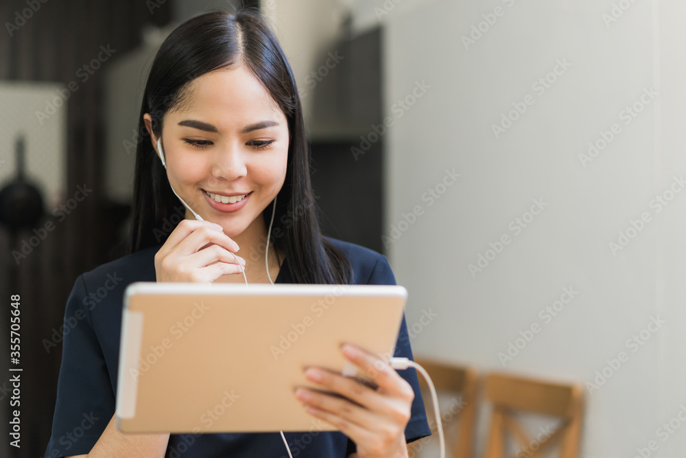 Beautiful asian women conferencing work from home with tablet taking on headphones in the morning. Smiling charming happy young female stay at home.