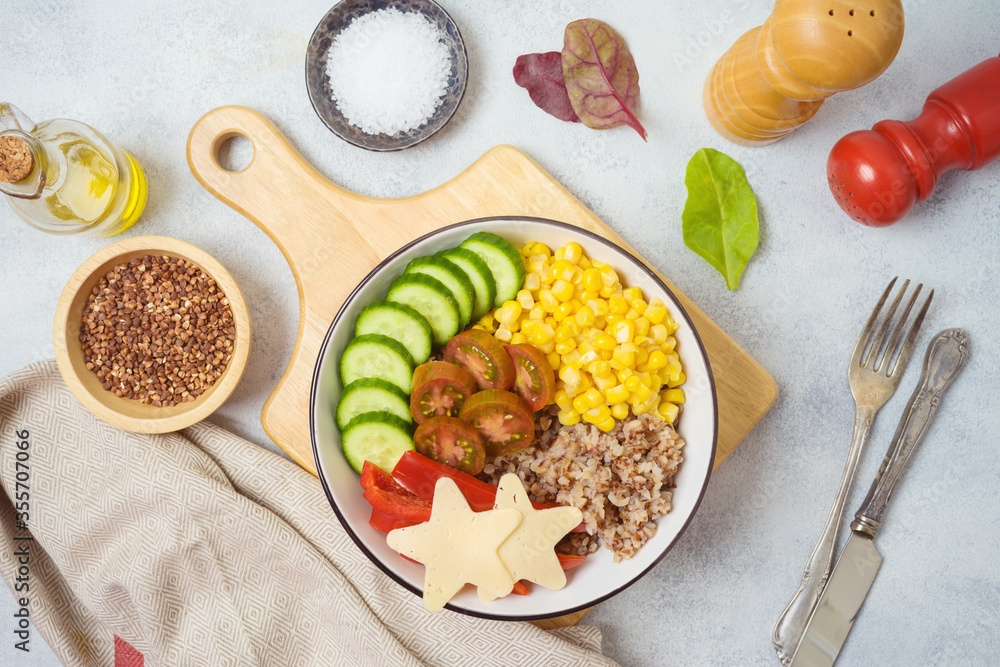 Buddha bowl with buckwheat, tomatoes, cucumber, red sweet pepper, corn and cheese on rustic table. Top view from above