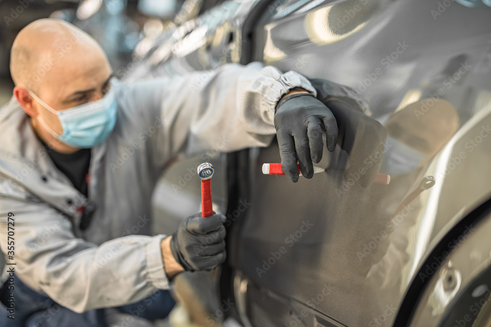 An employee of a car plant wearing a protective medical mask eliminates a small metal defect An employee of a car plant wearing a protective medical mask eliminates a small metal defect